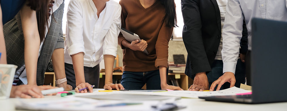Group of people standing around a table with documents and charts lying atop the table